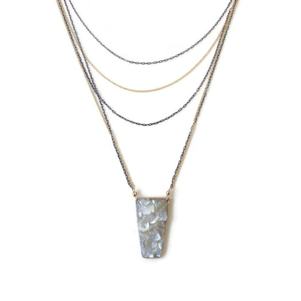 Five strand necklace on white background. Necklace chains alternate between oxidized silver and gold filled. A trapezoid pendant filled with crushed mother of pearl is attached to the two lowest chains of gold and silver. 