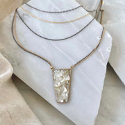 Five strand necklace on pieces of broken white marble with a piece of linen draped in the bottom corner. Necklace chains alternate between oxidized silver and gold filled. A trapezoid pendant filled with crushed mother of pearl is attached to the two lowest chains of gold and silver. 