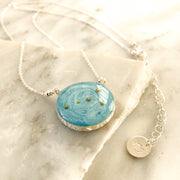 Image with a necklace placed on broken pieces of marble. Sterling silver necklace with sky blue background and the Cancer constellation made of gold beads. Custom stamping across the pendant reads “cupcake forever”. Jewelry tag with Cancer symbol is attached to the adjustable chain of the necklace