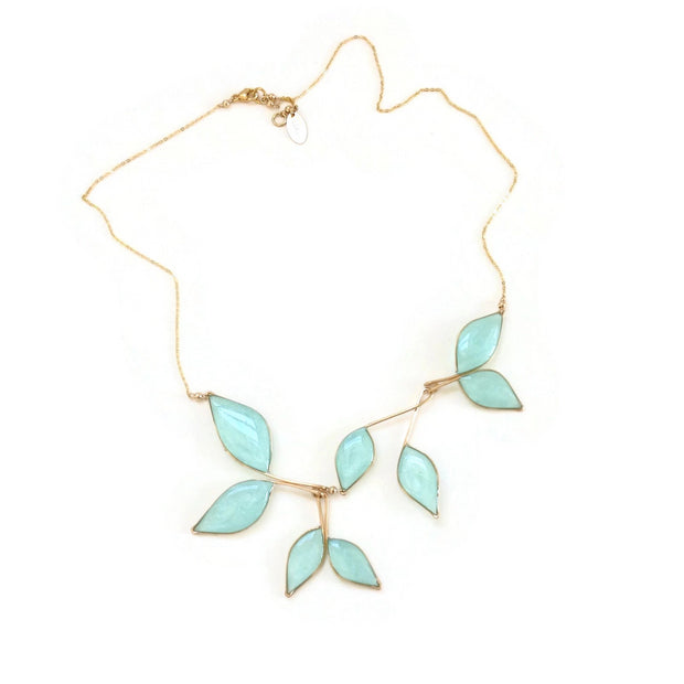 Gold necklace with 8 hanging leaf shaped pendants filled with clear sky blue resin with subtly  sparkling mica. Necklace is laying flat on a white background, showing its adjustable length chain and clasp. 