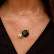Model wearing night sky constellation pendant on gold chain layered with a brass aquarius constellation coin wearing a black shirt.