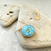Image with a necklace placed on a stone with slate background. Gold filled necklace with sky blue background and the Orion constellation made of gold beads.