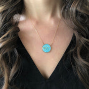 Model wearing a sky blue gemin constellatin necklace with a black v neck top framed by curled brown hair